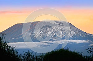 Landscape of snowy Kibo volcanic cone of Mount Kilimanjaro at sunset with colorful sky and clouds
