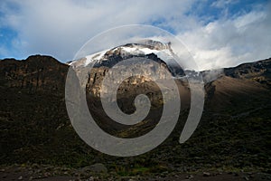 Landscape of a snowy peak of Mount Kilimanjaro covered with clouds under sunlight and shadow