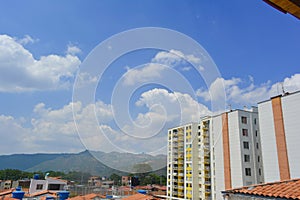 A landscape of some houses seen from the roof and yellow building wall with a blue sky in the background