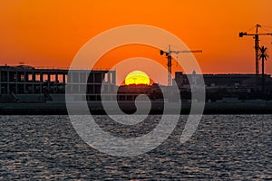 Landscape of sun rising over the construction site with crane in the sea in the morning in Dammam, Kingdom of Saudi Arabia