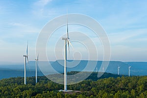 Landscape sun set shot of Wind turbines farm on the green grass field with clear blue sky and mountain at the background.