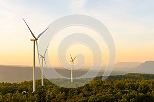 Landscape sun set shot of Wind turbines farm on the green grass field with clear blue sky and mountain at the background.