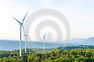 Landscape sun set shot of Wind turbines farm on the green grass field with clear blue sky and mountain at the background.