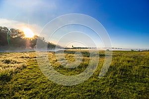 Landscape with sunrise from behind the forest over the river with fog.