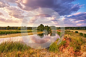 Landscape with sunset over river. Evening with Dramatic beautiful clouds on sky. Water reflection. Trees on riverbank. Weather