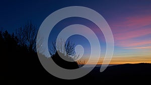 Landscape at sunset with a small moon. Silhouette of trees and mountains.