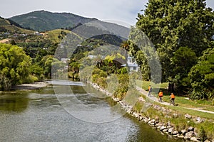 Landscape with three recreational cyclists in orange clothes alongside the river in Nelson, New Zealand