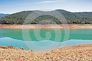 Landscape of the Tranco reservoir with its turquoise green water and its clay soil, the reflection of the pines on the calm water photo