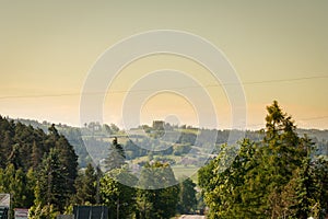 Landscape of trees and green grass, and in the background a view of the Polish Tatra mountains during sunset.