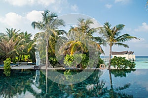 Landscape of tropical beach with infinity swimming pool and palm trees at island luxury resort