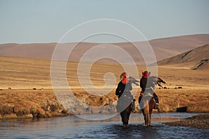 Landscape of two horseriders in a river surrounded by a deserted valley and mountains