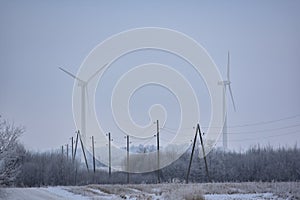 Landscape of two large white wind turbines in mist with electricity power lines at winter