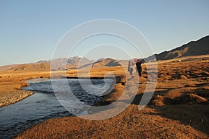 Landscape of a valley with a river and two horseriders with rocky mountains on a blurry background