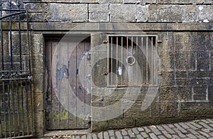 Landscape view of an ancient distressed wooden door with peeling paintwork, and a stone surround, and cobbled street