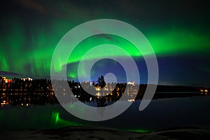 A landscape view of aurora borealis with a city scape under starry clear sky and reflection from lake water