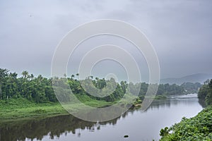 A landscape view of a calm river with green trees and mountain in India