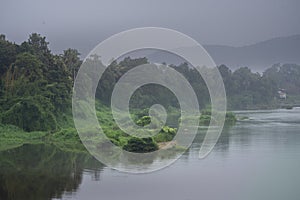 A landscape view of a calm river with green trees and mountain in India