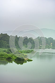 A landscape view of a calm river with green trees and mountain in India