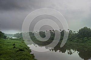 A landscape view of a calm river with green trees and mountain in India