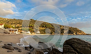 landscape view of Cavoli Beach on Elba in warm evening light and boulders in the foreground