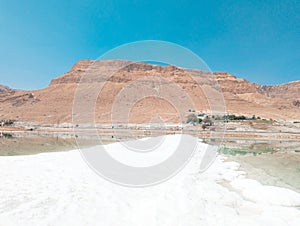 Landscape view on Dead Sea salt crystals formations, clear cyan green water and mountains at Ein Bokek beach, Israel