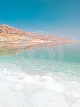 Landscape view on Dead Sea salt crystals formations, clear cyan green water and mountains at Ein Bokek beach, Israel