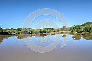 Landscape view of a lake surrounded by mountains and green savanna grassland, Pilanesburg Nature Reserve