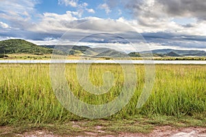 Landscape view of a lake surrounded by mountains and green savanna grassland, Pilanesburg Nature Reserve