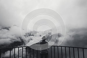 Landscape view of misty autumn mountain hills covered with fog and man silhouette in a hood. Monochrome photo