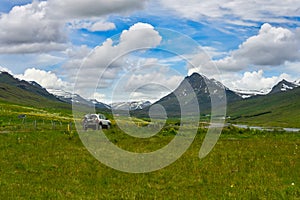 Landscape view of mountains and green grass in fresh and bright summer, white car running on Icelandic countryside road