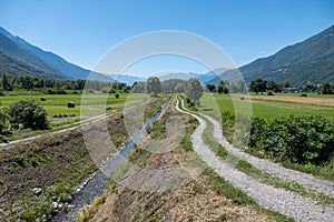 Landscape view of a narrow river in a rural field with hills in the background against a blue sky