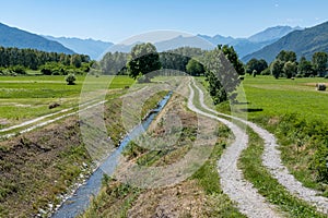 Landscape view of a narrow river in a rural field with hills in the background against a blue sky