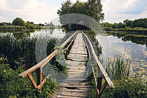 Landscape view of Old small wooden bridge across the lake. Fishman house on an island surrounded by wather and forest