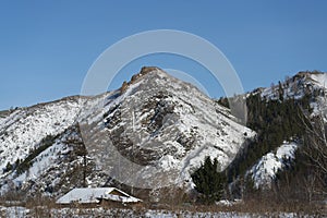 A landscape view of the rock at the top of the mountain with a hut at the foot of the mountain.