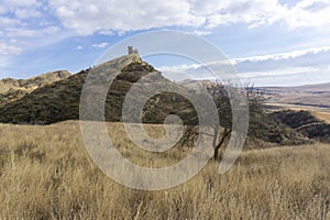 Landscape view of savanna and mountains. Stone tower on the hill above monastery. Dry orange grass and tree. Blue sky with clouds