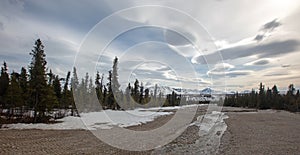 Landscape view of snowcapped mountains and gravel creekbed under lenticular clouds in the spring in Denali National Park