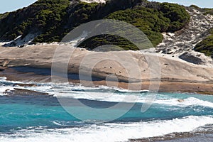 Landscape view of waves breaking over smooth granie rocks at Blue Haven Beach near Esperance in Western Australia under a bright