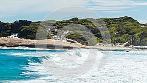 Landscape view of waves breaking over smooth granie rocks at Blue Haven Beach near Esperance in Western Australia under a bright