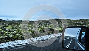Landscape of a volcanic lava field with highway and reflection in the car mirror