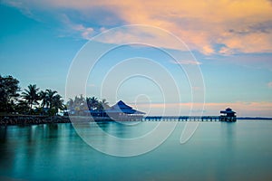 Landscape of water house on stilts, pontoon and palm trees at sunset