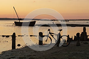 Landscape with water, old boat and bicicle at sunset photo