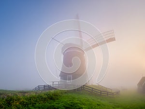 Landscape with windmill during fog. Holland. Dawn during a thick fog. Agricultural fields and pastures.