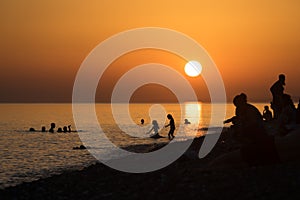 LandscapeCrowded beach at sunset, silhouetted against a bright orange sky.