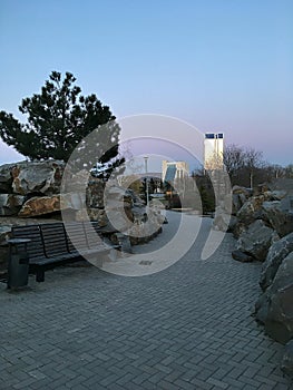 Landscaped park with decorative wild stones. Modern skyscrapers. Evening city.