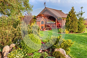 Landscaped summer garden with barbecue and wooden summerhouse Green trees, flowerbeds,