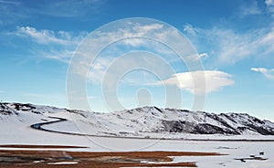 Landscaped in winter with country road and lenticular cloud on blue sky