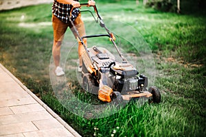 Landscaping concept - worker, gardener working with lawnmower and cutting grass in garden