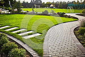 Landscaping of the garden. path curving through Lawn with green grass and walkway tiles.