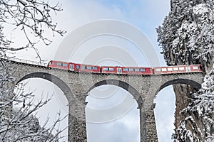 The Landwasser Viaduct with famous train of red color at winter time, landmark of Switzerland, snowing, Glacier express photo