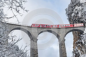 The Landwasser Viaduct with famous train of red color at winter time, landmark of Switzerland, snowing, Glacier express photo